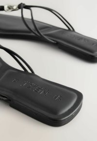 Sandales plates noires avec fines lanières et semelles carrées rembourrées, affichant la taille 37 et la marque "NEXT" embossée sur la semelle intérieure.