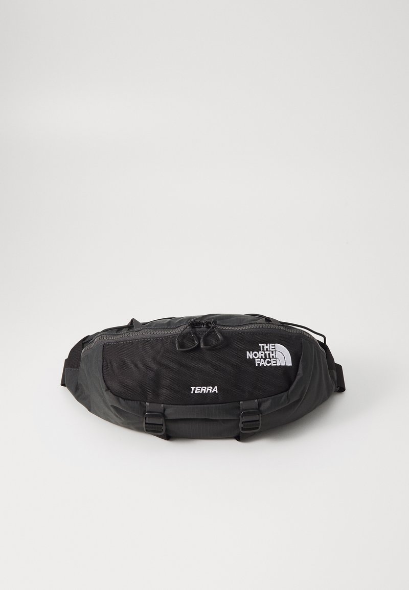 Borsetă neagră din material nylon durabil, cu un buzunar cu fermoar cu două capete și un logo și text alb contrastant. Design compact cu bretele ajustabile.