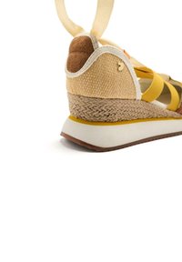 Sandale compensée jaune et beige avec une texture tissée, des brides en tissu et une semelle en caoutchouc. Possède un lien en tissu et un petit logo sur le talon.