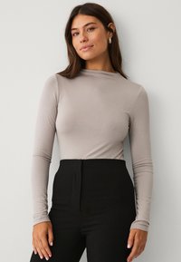 Hellgraues Langarmshirt aus weichem Stoff mit hohem Kragen, kombiniert mit hochgeschnittenen schwarzen Hosen, die eine figurbetonte Silhouette präsentieren.