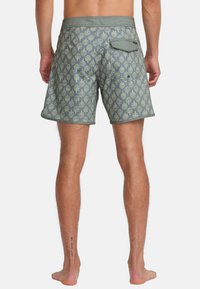 Bañadores de hombre, azul-verde con un patrón de árboles, cintura elástica, bolsillo trasero único con solapa y botón, y una textura suave.