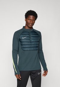 Marine langermet Nike genser med polstret brystseksjon, kvart glidel�ås og lysegule detaljer på ermene. Glatt stoffstruktur.