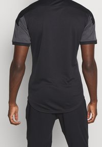 Black athletic shirt with short geometric patterned sleeves, a fitted design, and a smooth texture. Contrast stitching along the hem.