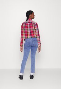 Camisa xadrez vermelha e verde com colarinho, combinada com jeans de brim azul claro. A modelo está de costas para a câmara, usando sapatos pretos.