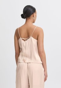 Blush satin camisole dengan tali spaghetti, desain belakang yang diikat, dan aksen manik-manik. Tekstur halus dengan potongan santai dan hem berlapis.