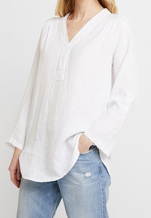 Witte linnen blouse met een V-hals, lange mouwen en een knopenlijst. Heeft een losse pasvorm en een subtiele textuur. Gecombineerd met licht denim.