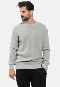 Pull en maille côtelée gris clair avec un col rond et des manches raglan. Présente un accent noir sur la manche gauche et des poignets ajustés.
