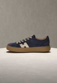 Baskets basses bleu marine avec semelle marron, lacets blancs et logo blanc en forme de H sur le côté, affichées sur fond gris.