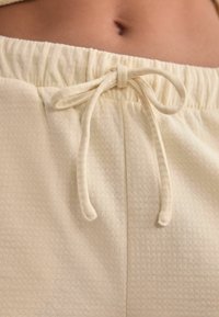 Helle beige Drawstring-Shorts aus strukturiertem Stoff. Verfügt über einen elastischen Bund und eine gebundene Schleife an der Vorderseite.