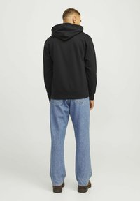 Black hoodie with a wide, adjustable hood, paired with light blue, wide-leg jeans. The fabric appears soft with a smooth texture.