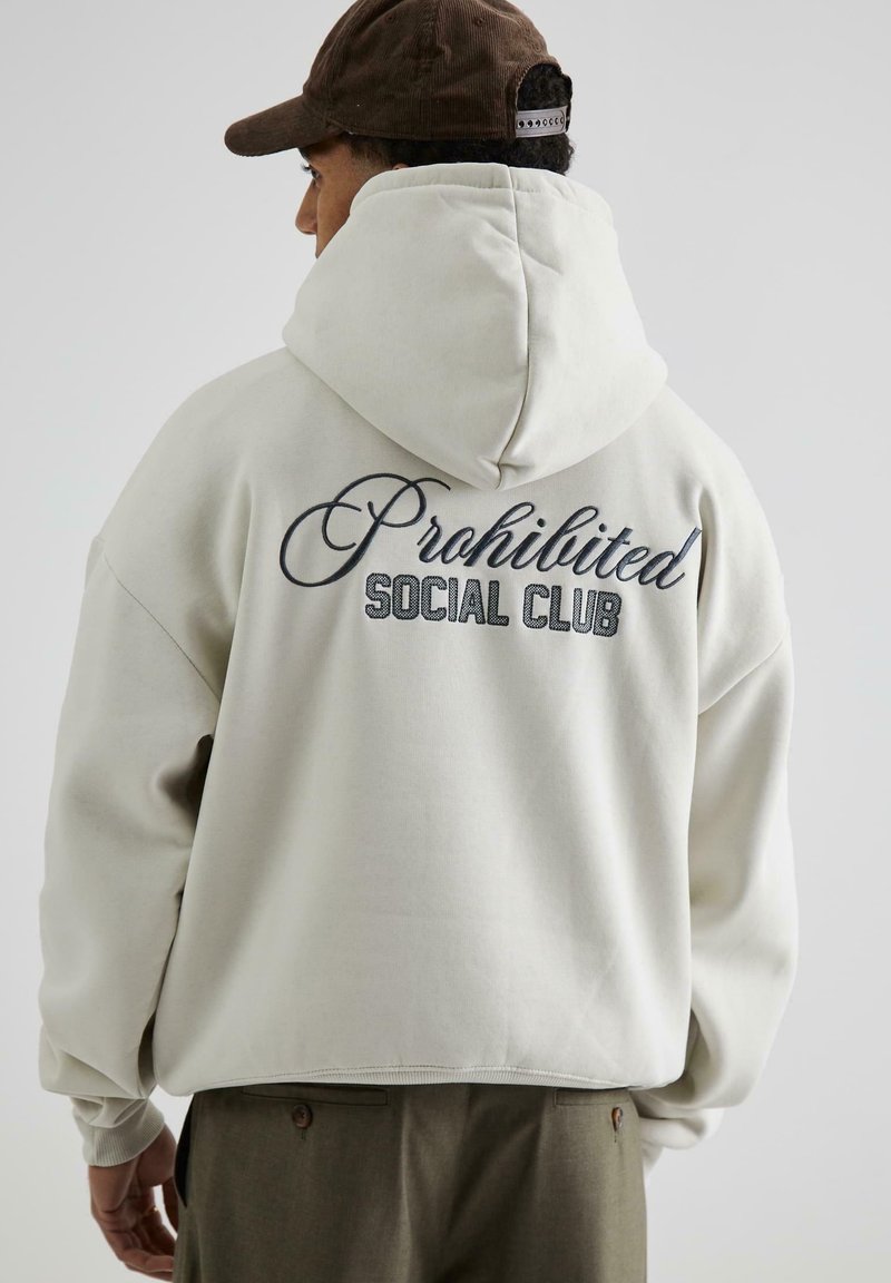 Felpa leggera beige con una grande scritta "Proibito" ricamata in corsivo e "SOCIAL CLUB" in lettere maiuscole sulla schiena. Tessuto morbido, vestibilità comoda.