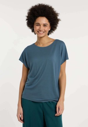 Top blu con maniche corte, dalla vestibilità ampia e rilassata e con una texture morbida; abbinato a pantaloni ampi color turchese, entrambi su uno sfondo chiaro.