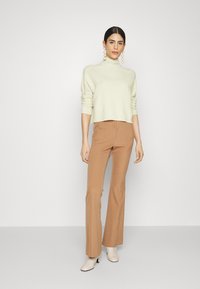 Hellgrüner, cropped Pullover mit umgeschlagenen Bündchen. Braune, weit geschnittene Hose mit eingearbeiteten Falten. Beigefarbene Stiefeletten runden das Outfit ab.