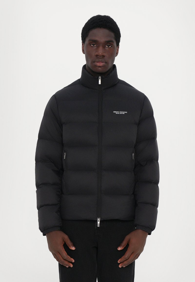 Schwarze Pufferjacke mit hohem Kragen, leicht, stepptexturiert, durchgehender Reißverschluss vorne und seitlichen Reißverschlusstaschen. Logo auf der Brust.