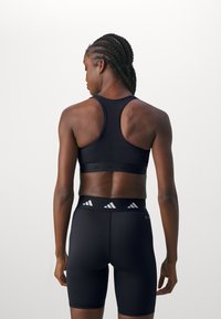 Svart sports-BH med racerback-design og elastisk bånd, i kombinasjon med høyhårede svarte shorts som har Adidas-logo på midjebåndet.