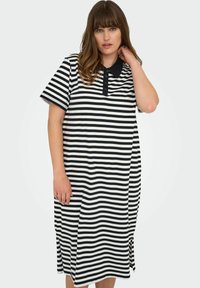 Pruhované šaty v černé a bílé barvě s límečkem, krátkými rukávy a bočními rozparky pro snadnější pohyb.