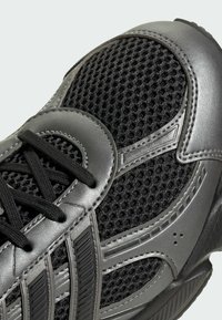 Čierna športová obuv s mesh vrchom, lesklými sivými akcentmi, textúrovanými prekrytiami a plochými čiernymi šnúrkami na odpruženej podrážke.