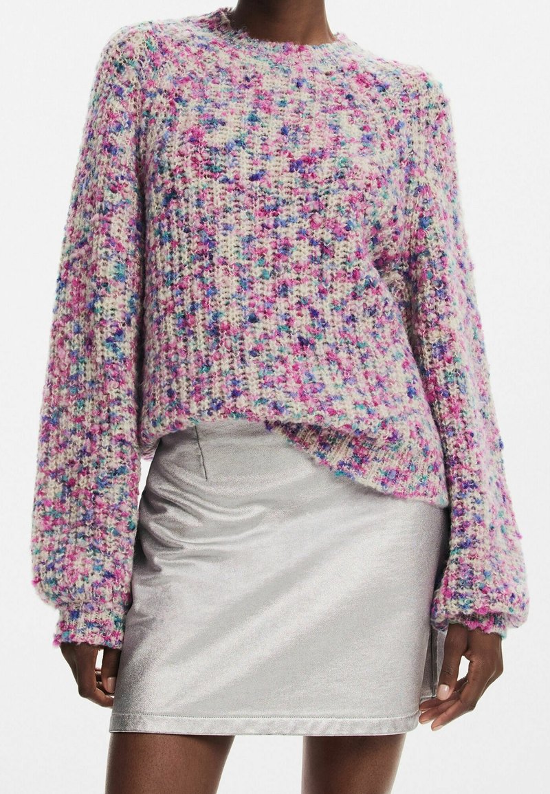 Pull en maille aux fibres multicolores avec des nuances de rose, bleu et crème, présentant un col rond et des manches longues et volumineuses. Associé à une jupe argentée.