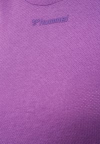 Fioletowa koszulka sportowa z teksturowanej dzianiny. Logo "hummel" jest wytłoczone na piersi. Projekt jest prosty i dopasowany.