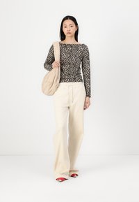 Camisa de leopardo de manga larga combinada con pantalones anchos crema y sandalias rojas de punta abierta. Llevando un bolso de hombro beige suave.