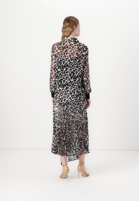 Durchsichtiges Leopardenmusterkleid mit langen Ärmeln, plissiertem Rock und schwarzen Manschettendetails. Das transparente Material hebt die darunterliegende Haut hervor.