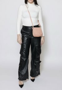 Pantaloni cargo neri in finta pelle con molteplici tasche, abbinati a un dolcevita bianco a maniche lunghe e a una borsa a tracolla rosa chiaro.