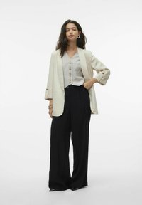 Igapäevane riietus, mis sisaldab heledat beeži bleiserit, halli varrukateta topi nupudega ning musti laiad jalad pükse, kõik sujuvatest kangastest.