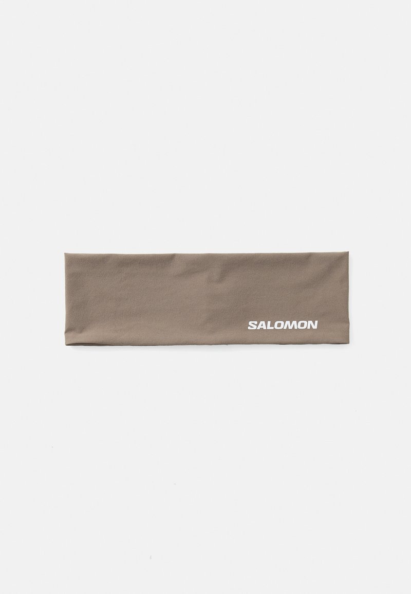 Brun stoffhodebånd med en jevn tekstur. Har hvit "SALOMON"-logo på den ene siden. Rektangulær form, passende for utendørsaktiviteter.