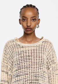 Strickpullover mit lockerem, offenem Maschenmuster in Creme, ausgestattet mit weitem Ausschnitt, überschnittenen Schultern und subtilen horizontalen Streifen.