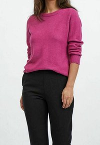 Rosa, långärmad tröja med rund halsringning, ribbade ärmslut och nederkant, tillsammans med svarta, figurnära byxor. Mjuk stickad textur.