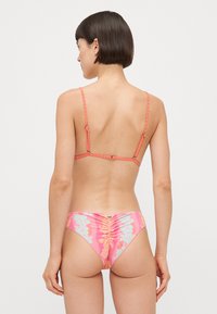 Bikini set featuring a pink floral pattern with turquoise accents. The top has thin adjustable straps, and the bottom has ruched detailing.