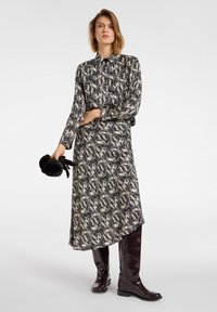 Tištěné midi šaty v černé a krémové barvě s límečkem, dlouhými rukávy a splývavým siluetou. Nosené s lesklými burgundskými kozačkami po kolena.