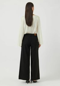 Breda svarta jeans i denim, kombinerat med en ljuskrämfärgad texturerad blus. Blusen har långa ärmar och en avslappnad passform.