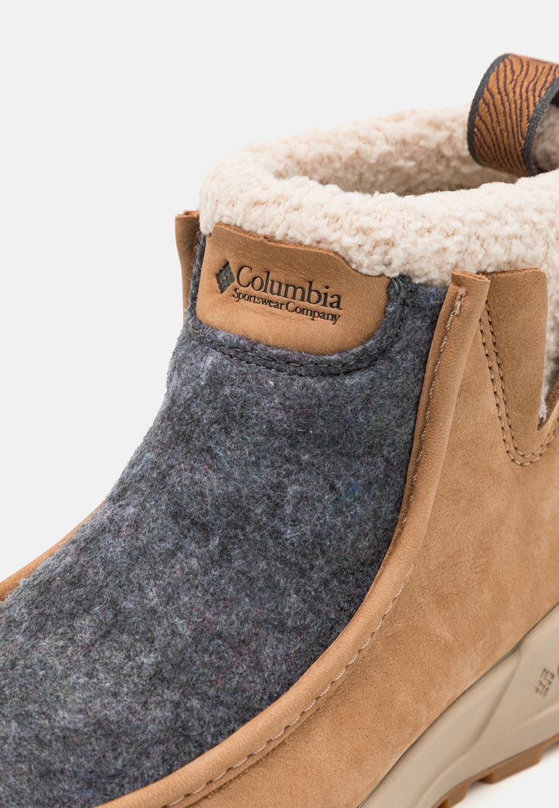 Botín de ante marrón con parte superior de fieltro gris, forro de crema esponjoso y parche con el logo de Columbia. Presenta una suela de goma resistente y acentos cosidos.