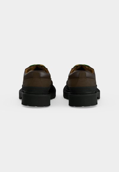 Paire de chaussures en cuir marron avec semelles épaisses en caoutchouc noir, vues de dos sur un fond clair uni.