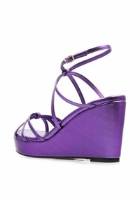 Sandalias de cuña moradas con acabado metálico. Presentan un diseño de tiras, correa de tobillo ajustable y tacón de cuña grueso. Textura suave.