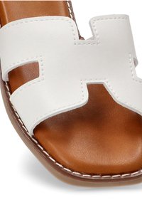Sandalia deslizante de cuero blanco con diseño recortado. Plantilla de cuero marrón, acentos cosidos y una textura suave en la parte superior.