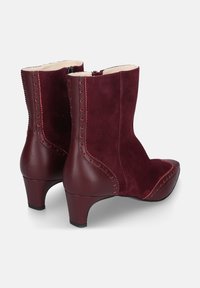 Bordeauxrode enkellaarzen van suède en leer, met een spits toelopende neus, een gebogen hak en decoratieve stiksels langs de naden.