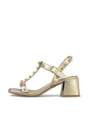Zlatá kožená sandála s blokovým podpatkem, kotníkovým páskem s přezkou a ozdobnými cvoky na páscích.