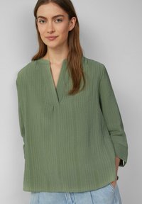 Hellgrünes, strukturiertes Blusenshirt mit lockerer Passform, V-Ausschnitt und drei Viertelärmeln, entworfen mit vertikalen Streifen und relaxed Silhouette.