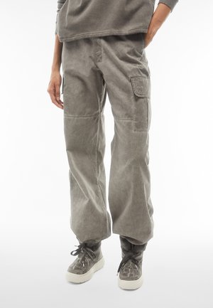 Pantalons cargo gris clair avec une coupe décontractée, dotés d'un tissu texturé, de poches latérales et de poignets élastiques. Portés avec des chaussures montantes grises.