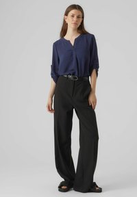 Marineblouse met een V-hals en driekwart mouwen, gecombineerd met hoogblijvende zwarte wijde broek en zwarte sandalen met een gesp.