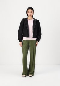 Black cropped jacket with a hood, paired with a light pink ribbed top and green pleated pants. The shoes are cream with a black accent.