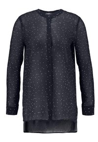 Tunn svart blus med långa ärmar, rak skärning, framknappar och vita stjärnliknande dekorationer över hela. Mjuk textur och lättviktigt tyg.