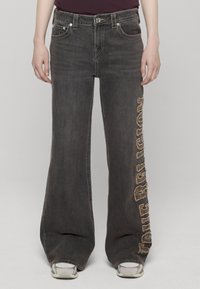 Pantalones vaqueros negros de pierna ancha con un adorno de logo desgastado en el lado izquierdo, con un diseño clásico de cinco bolsillos y herrajes metálicos.