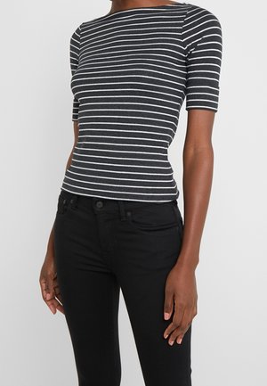 Schwarz-weiß gestreiftes Kurzarmoberteil mit Bootsausschnitt, figurbetontem Design und glatter Textur, kombiniert mit schmal geschnittenen schwarzen Jeans.