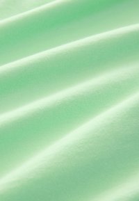 Hellgrüner Baumwollstoff mit einer glatten Textur, der weiche, fließende Falten und ein gleichmäßiges Webmuster aufweist.