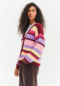 Swetrowy kardigan w prążki, wykonany z mieszanki wełny, w odcieniach bordowego, różowego, lawendowego i żółtego. Luźny krój z szerokimi rękawami i dekoltem w serek.