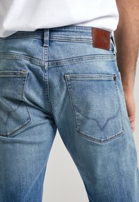 Jeans de mezclilla azul claro con corte ajustado, que presentan dos bolsillos traseros, costuras distintas y una etiqueta de cuero marrón en la cintura.