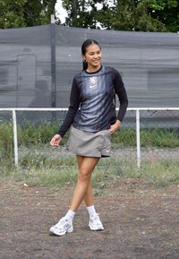 Athletic outfit with a black long-sleeve top featuring striped design and Nike logo, paired with a gray skirt and white sneakers. Outdoor setting.